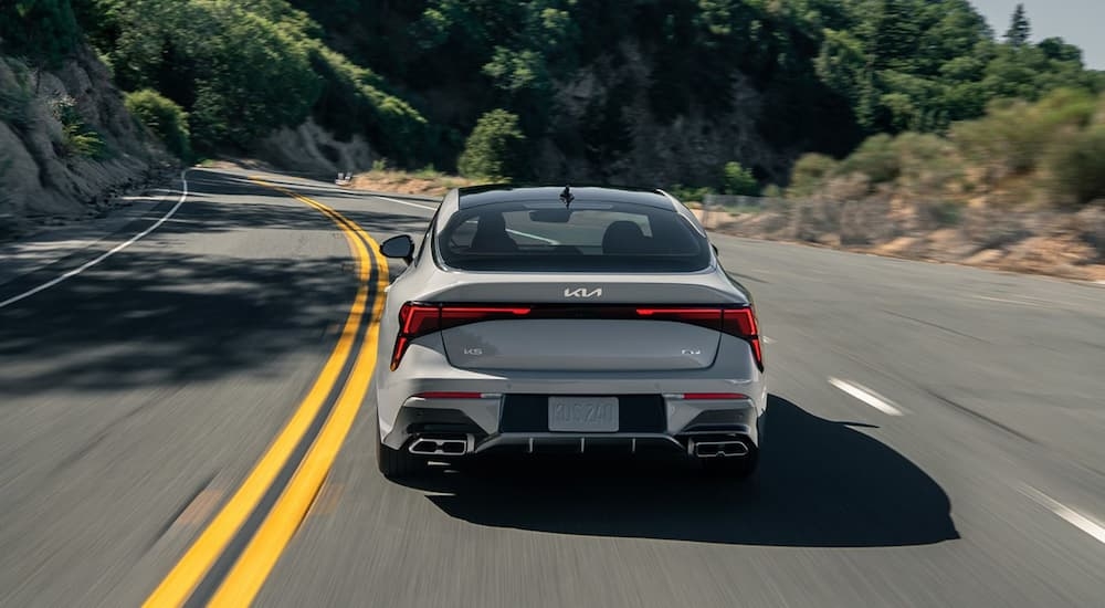 Rear of a grey 2025 Kia K5 GT driving on an open road.