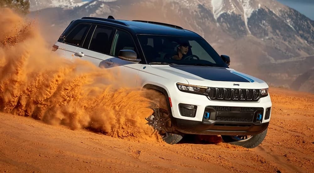 White 2024 Jeep Grand Cherokee 4xe driving down a desert hill.