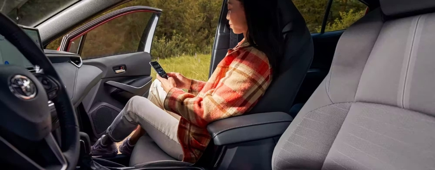 A person using a smart phone in a 2023 Toyota Corolla Hybrid SE.