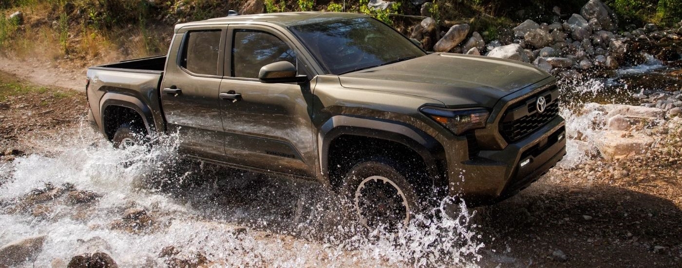 A green 2025 Toyota Tacoma TRD Off-Road splashing through a creek.