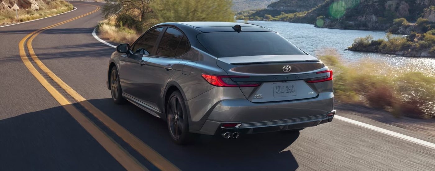Rear of a grey 2025 Toyota Camry XSE driving by a river.