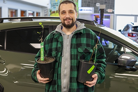Man in green flannel posing with two trees in pots