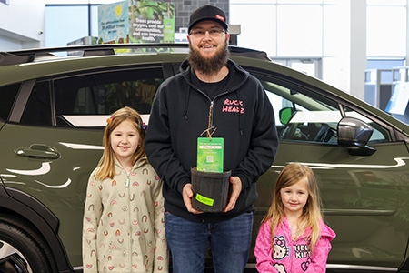 Man posing with his two young daughters while holding a potted tree
