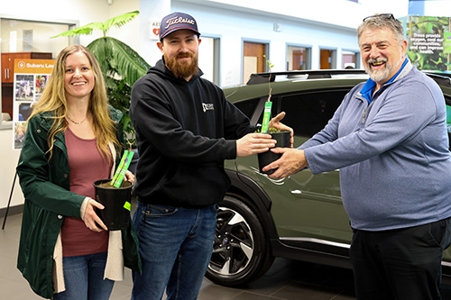 Man handing native tree in pot to a man and woman in the Spangler Subaru showroom