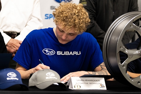 Student with Greater Johnstown Career and Technology Center who is wearing a blue Subaru shirt is signing and employment contract