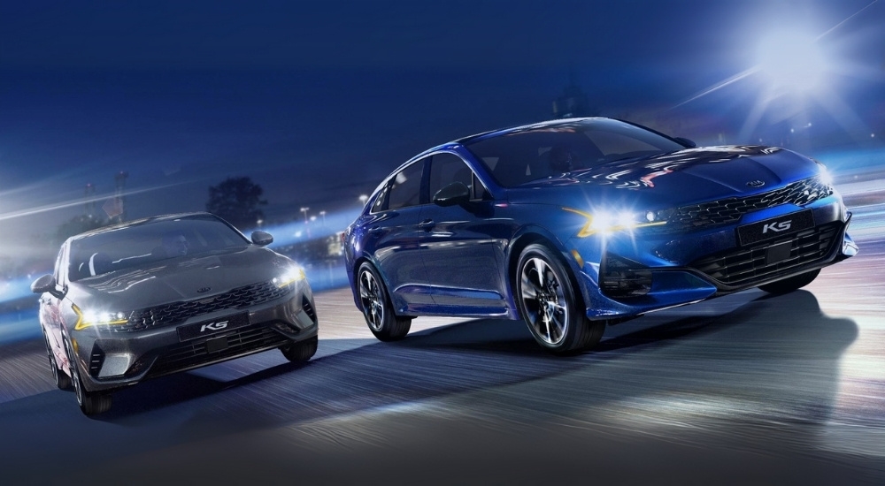 A grey and a blue 2021 Kia K5 driving at night.