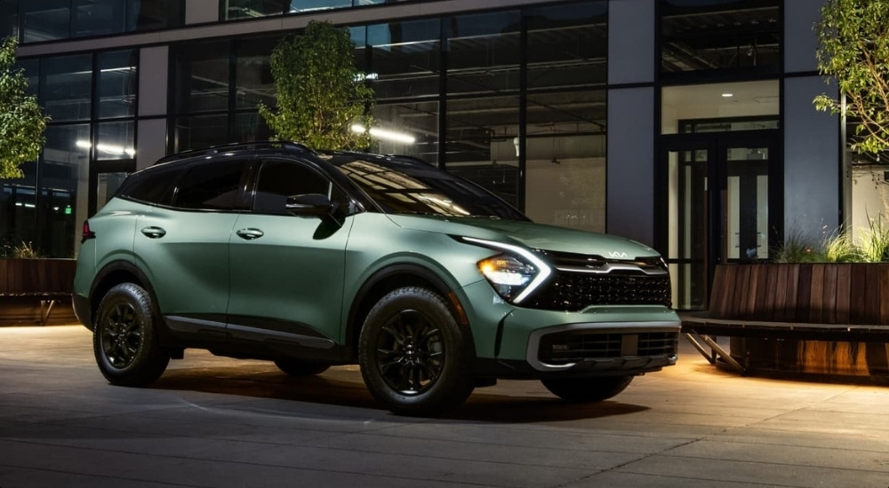 A green 2025 Kia Sportage X-Pro Prestige parked in front of a building.
