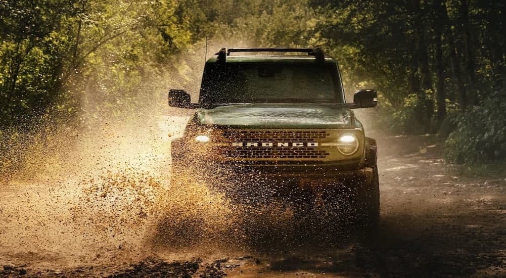 A green 2025 Ford Bronco driving through muddy water.