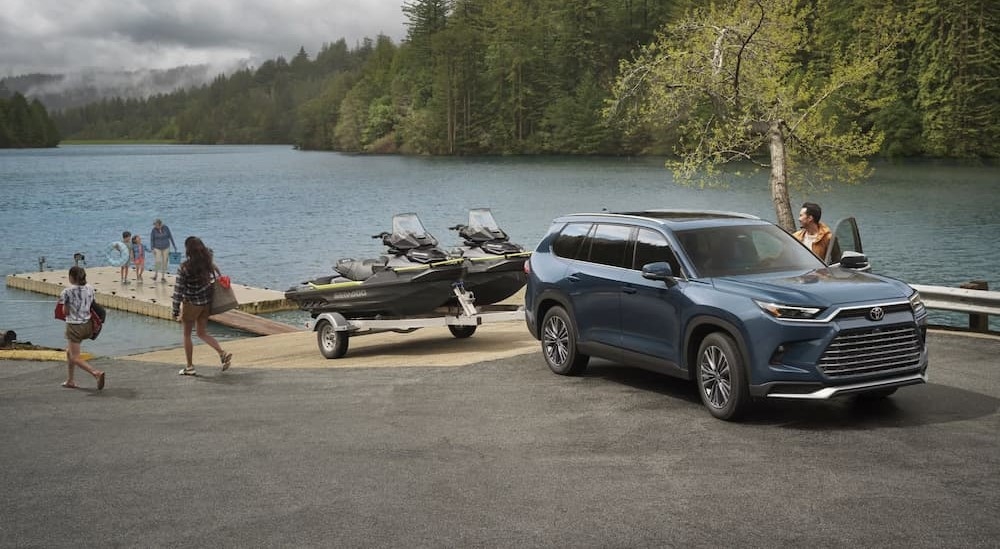 A blue 2025 Toyota Grand Highlander towing a trailer near a lake.