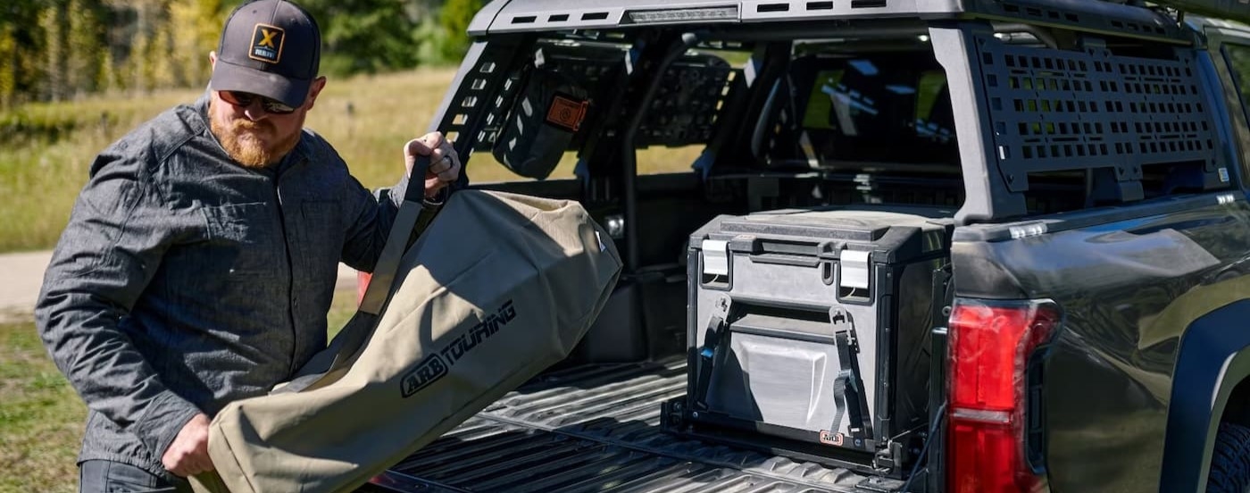 A person stowing gear in the bed of a black 2025 Toyota Tacoma.