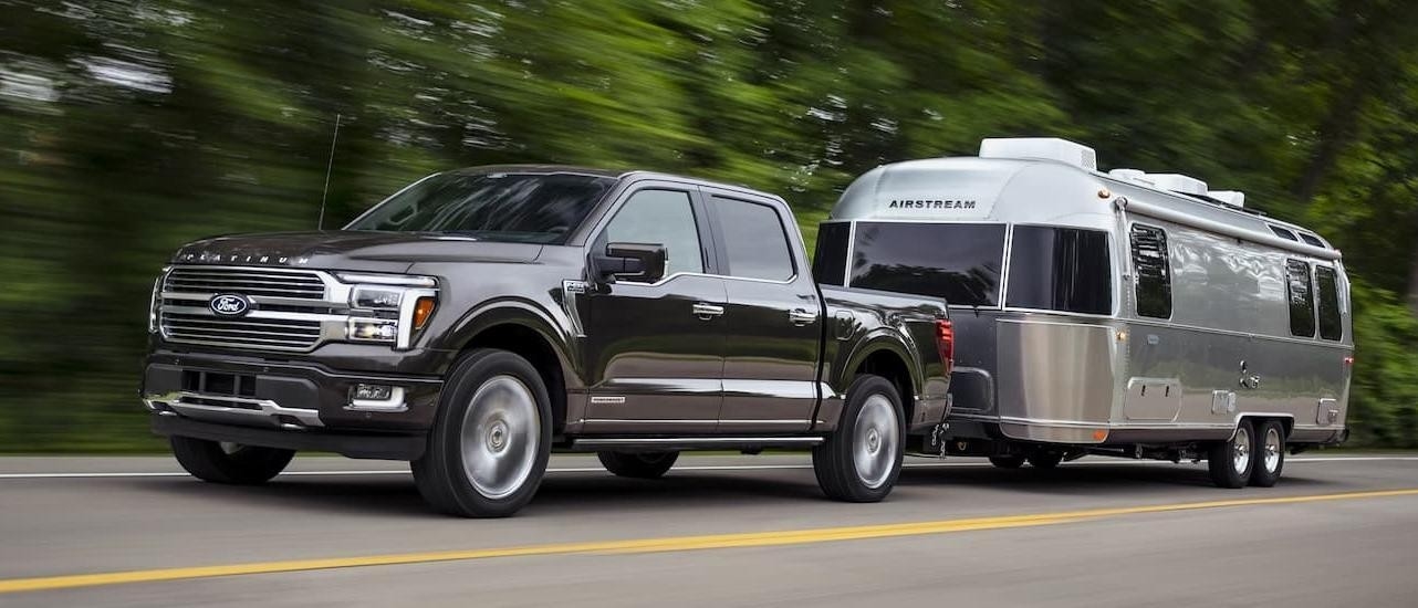 A grey 2025 Ford F-150 from the front while towing a camper.