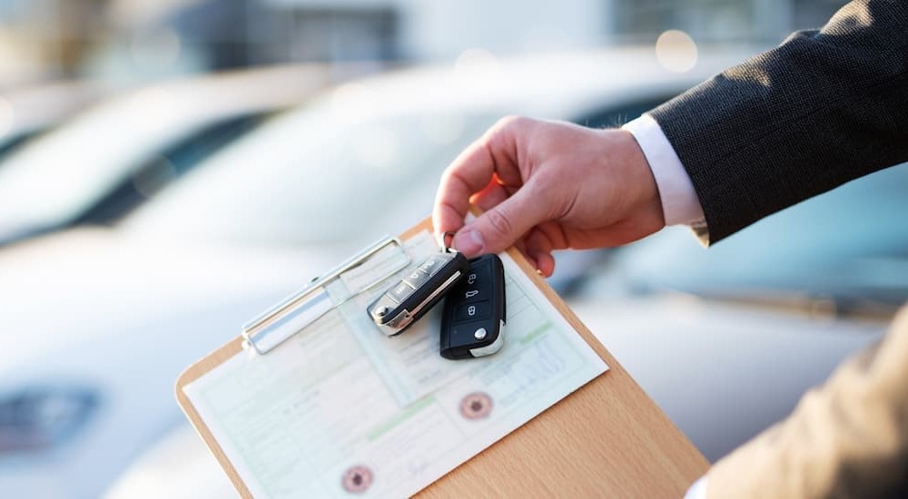 A person holding a clipboard with a registration attached and two key fobs. 