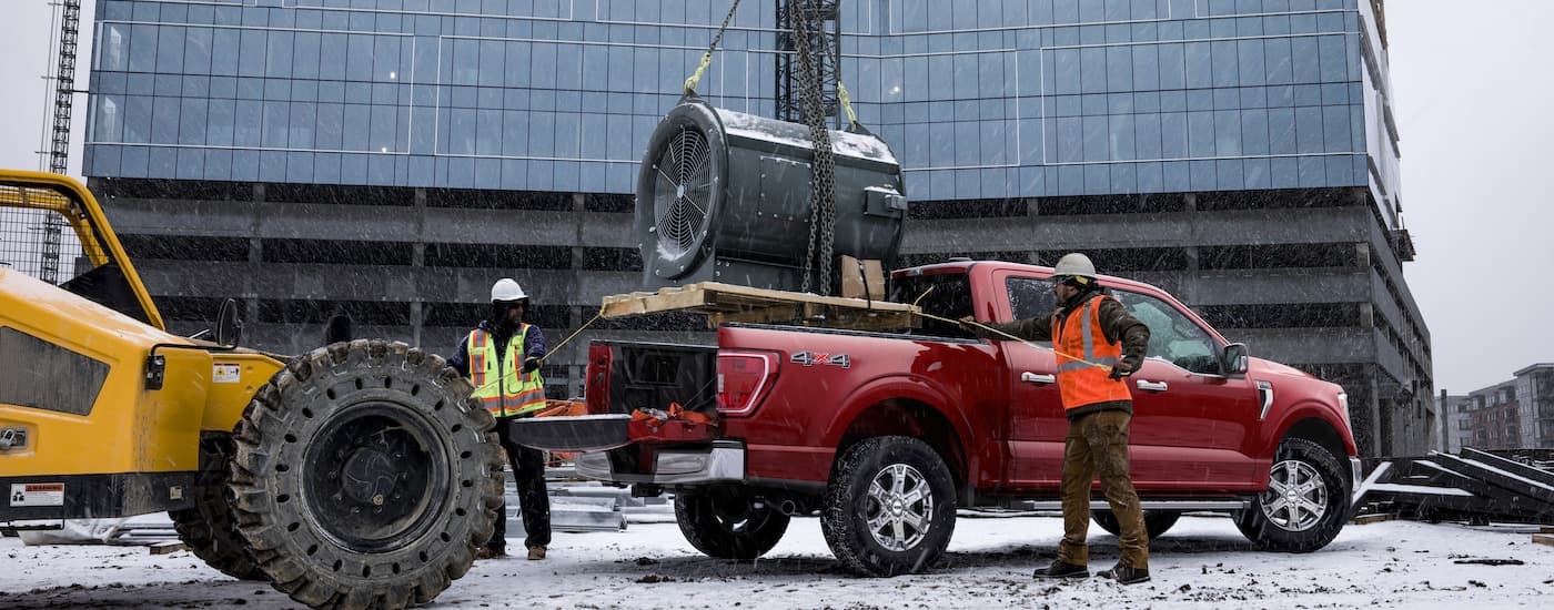 A red 2025 Ford F-150 from the side being loaded on a jobsite.