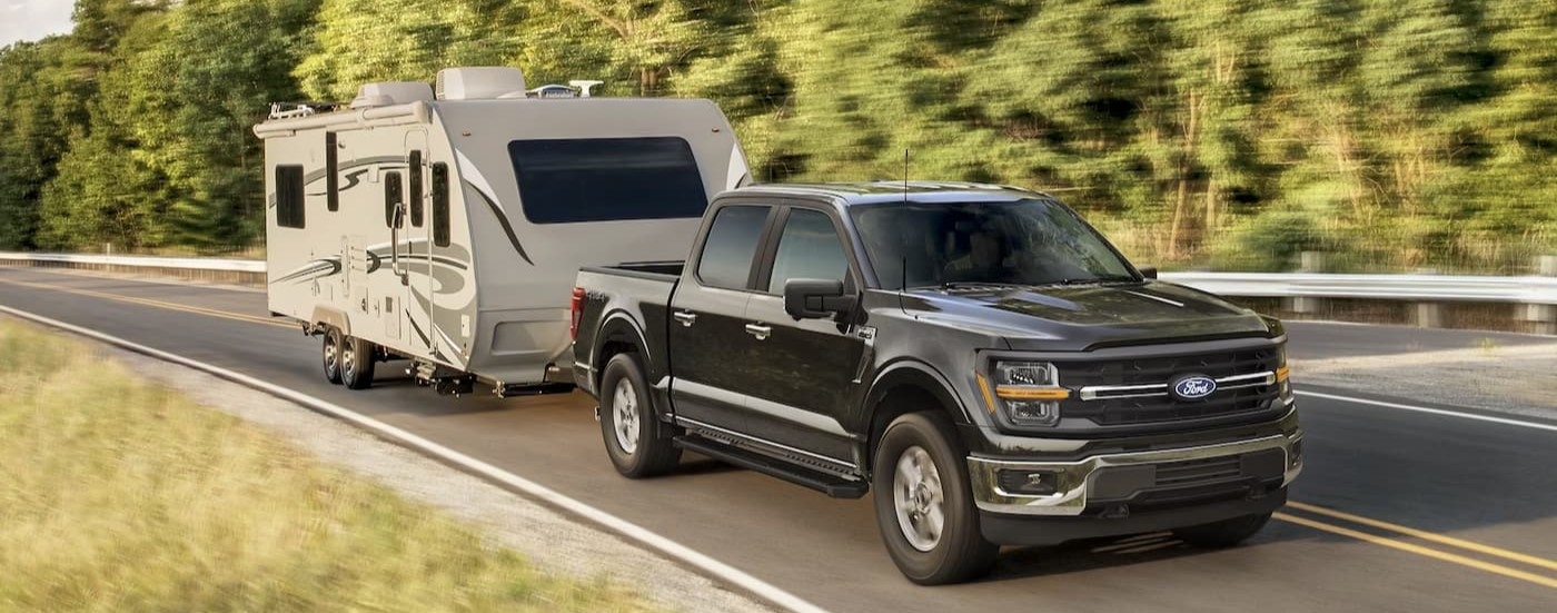 A black 2025 Ford F-150 towing a trailer on a highway.
