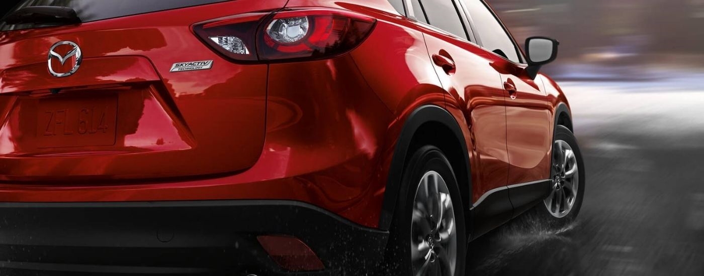 A red 2016 Mazda CX-5 driving on a wet road.