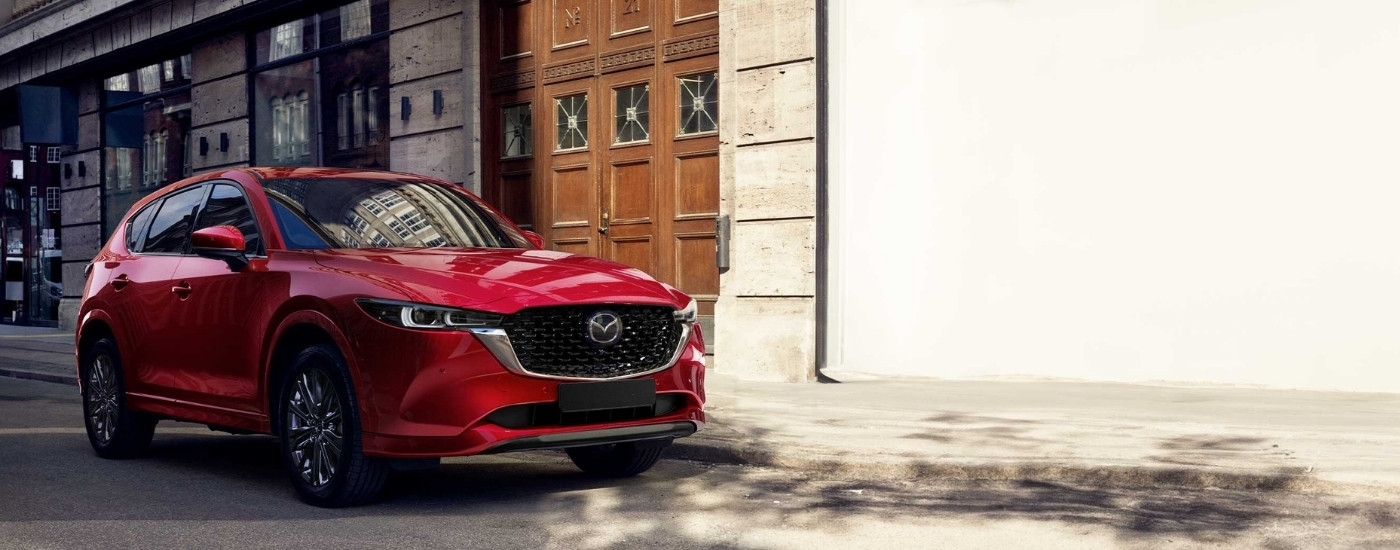 A red  2025 Mazda CX-5 for sale parked in front of a building.