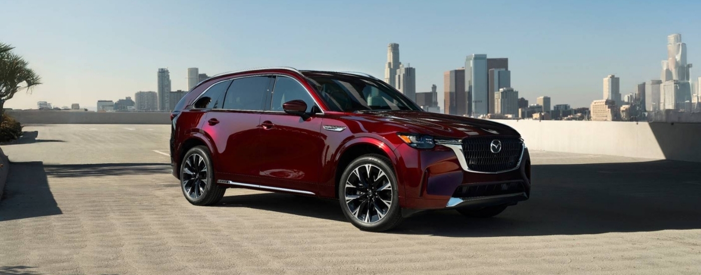 A purple 2025 Mazda CX-90 overlooking a city skyline.