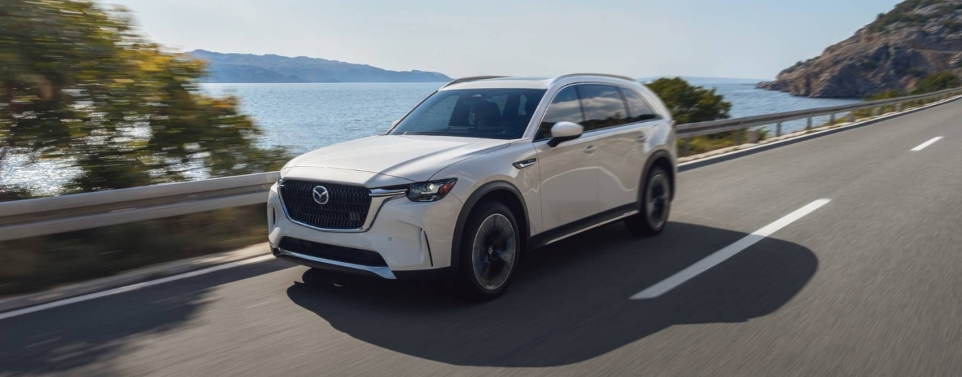 A white 2025 Mazda CX-90 PHEV driving past a bay.
