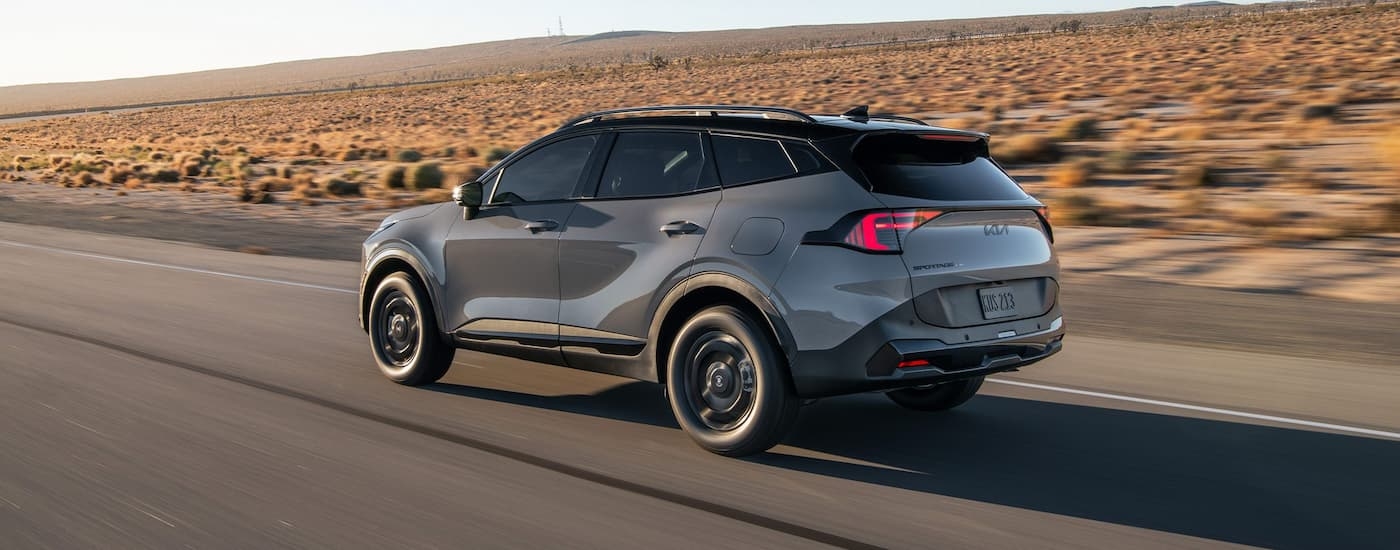 Grey 2026 Kia Sportage driving on an open road through a desert
