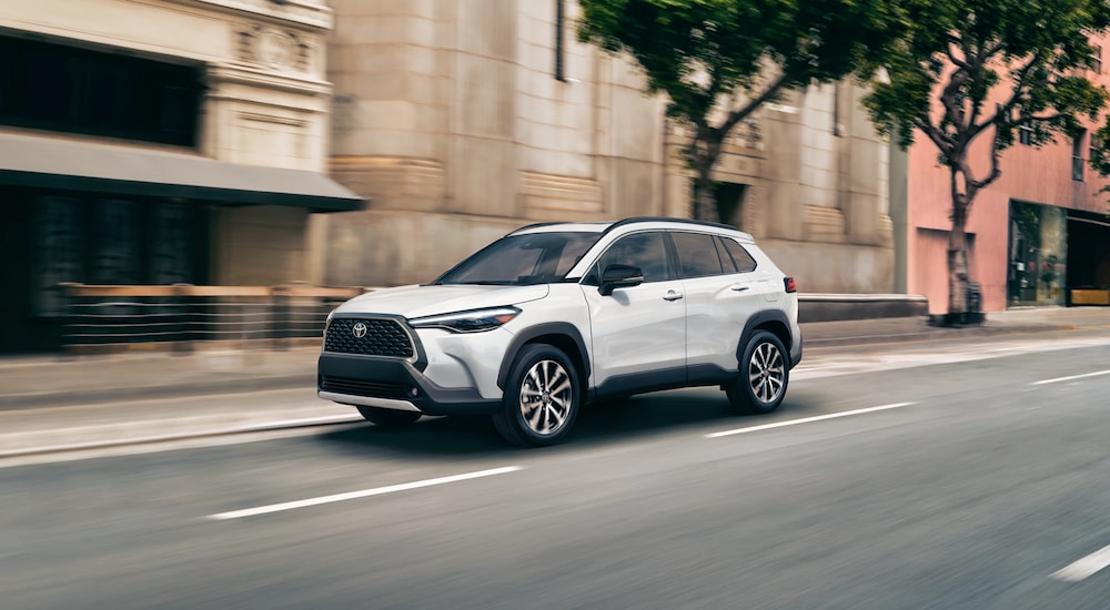 White 2025 Toyota Corolla Cross driving down a street.