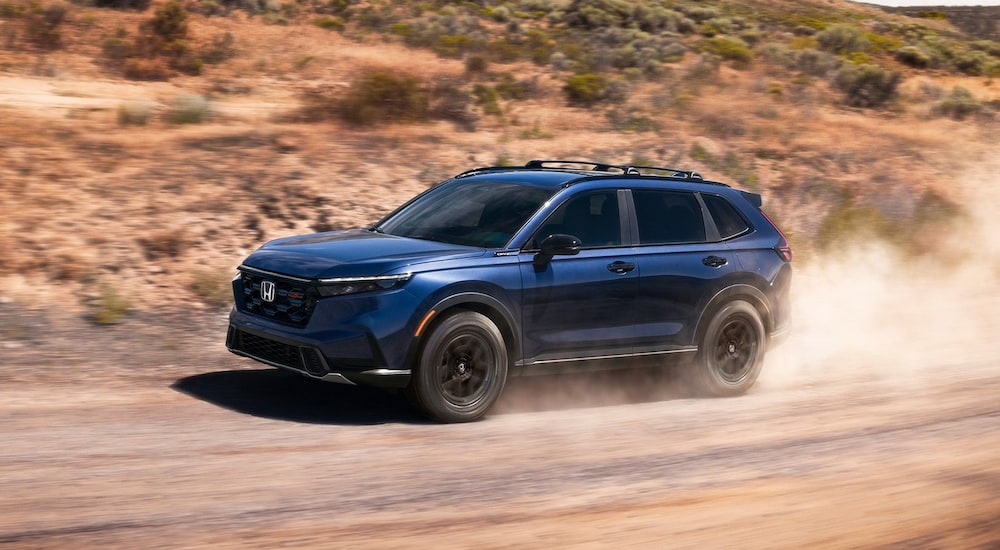 Blue 2026 Honda CR-V TrailSport Hybrid driving down a dirt road.