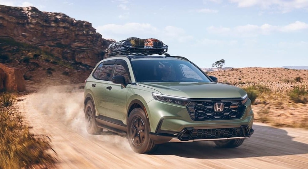 A green 2026 Honda CR-V TrailSport driving on a dirt road.