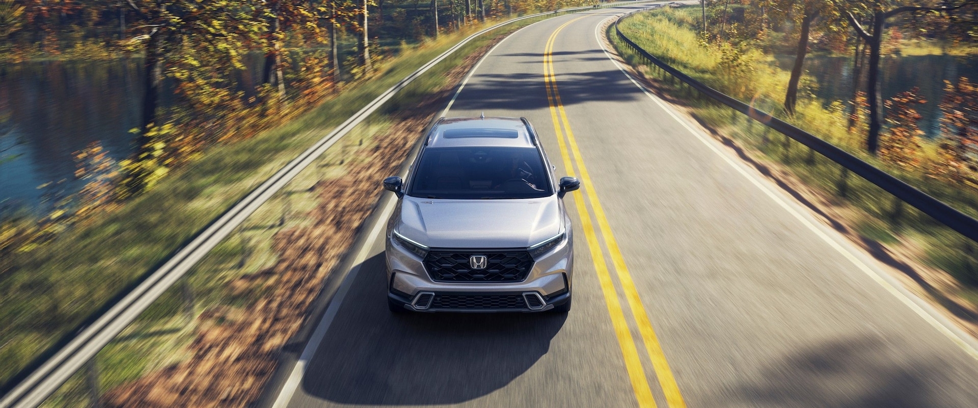 White 2026 Honda CR-V Sport Touring Hybrid driving down an open road.