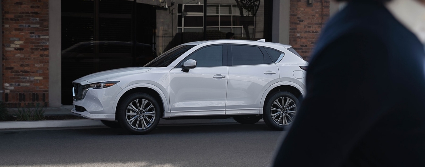A white 2025 Mazda CX-5 for sale near Coral Gables parked in front of a brick building.