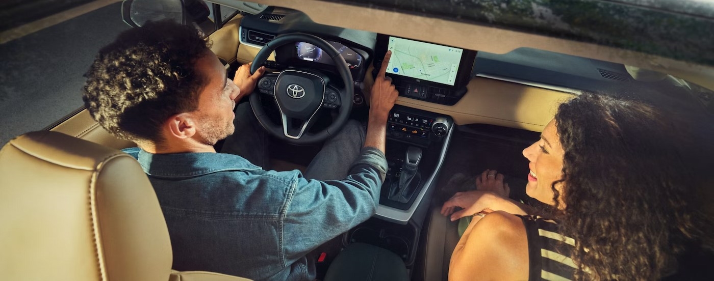 Two people driving in a 2025 Toyota RAV4 Hybrid for sale in Westminster.