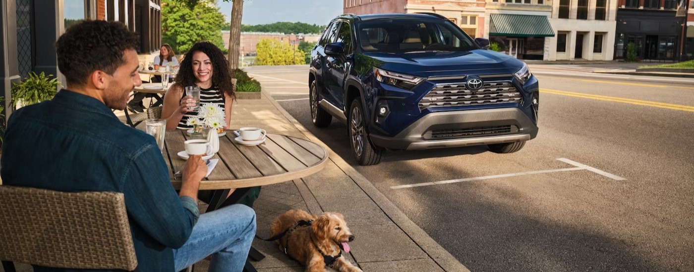 A blue 2025 Toyota RAV4 Hybrid parked near a cafe.
