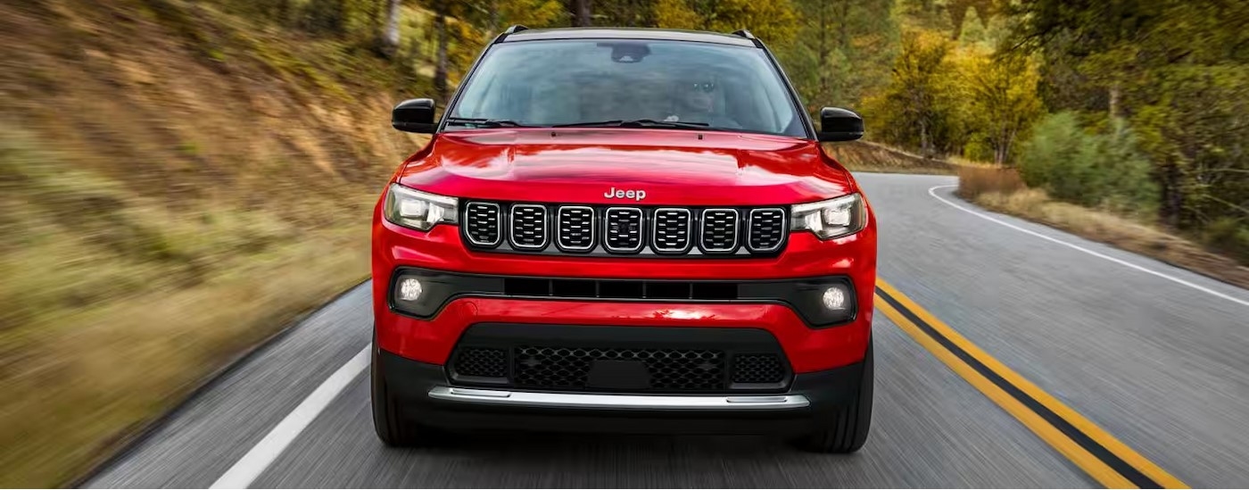 A red 2025 Jeep Compass driving on a highway.