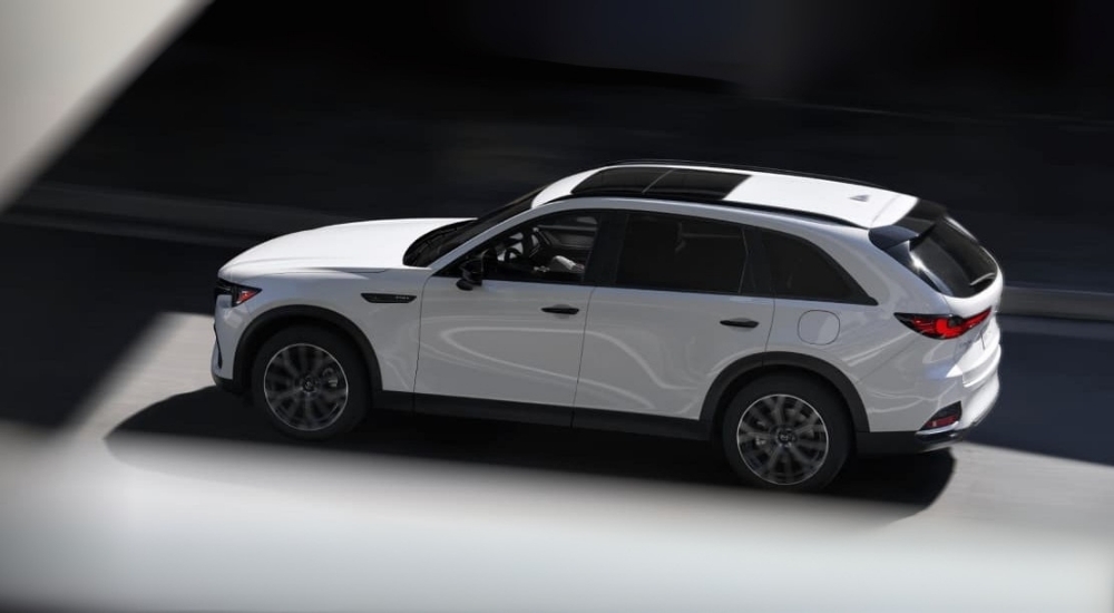A white 2025 Mazda CX-70 PHEV driving on a highway.