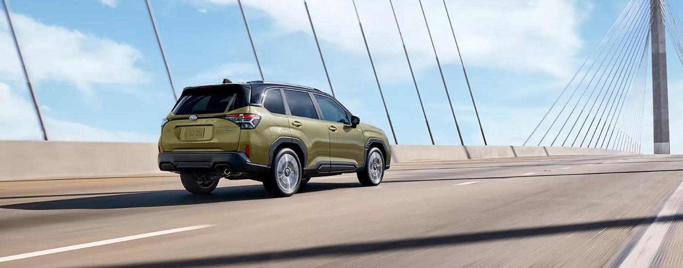 A green 2025 Subaru Forester Hybrid driving over a bridge.