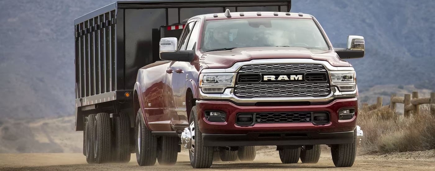 A red 2025 Ram 3500 is towing a large trailer on a dusty dirt road