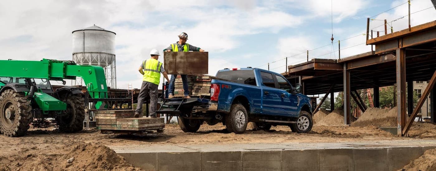 Workers loading boards into the bed of a blue 2020 Ford F-250 after visiting a used car dealer in Rhinebeck.
