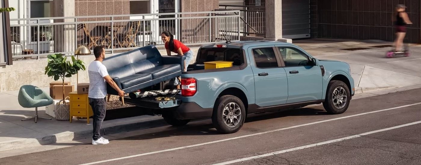 People loading furniture into the bed of a light blue 2022 Ford Maverick.