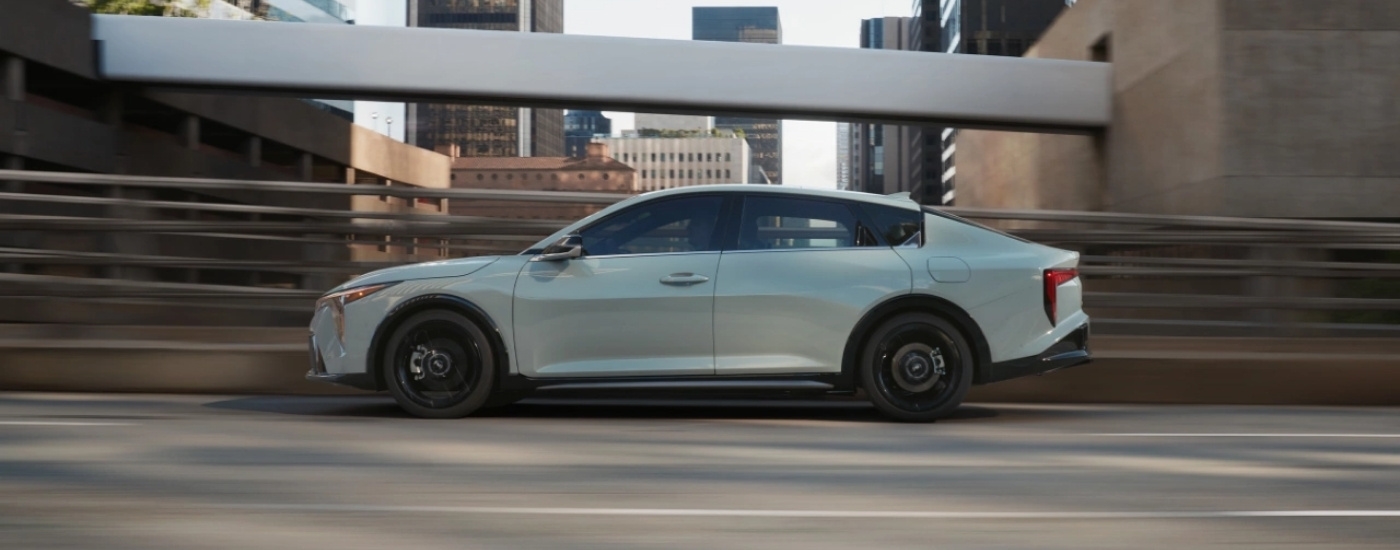 A grey 2025 Kia K4 driving past city buildings.