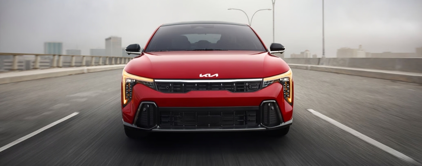 A red 2024 Kia K4 for sale near Tomball driving over a bridge.