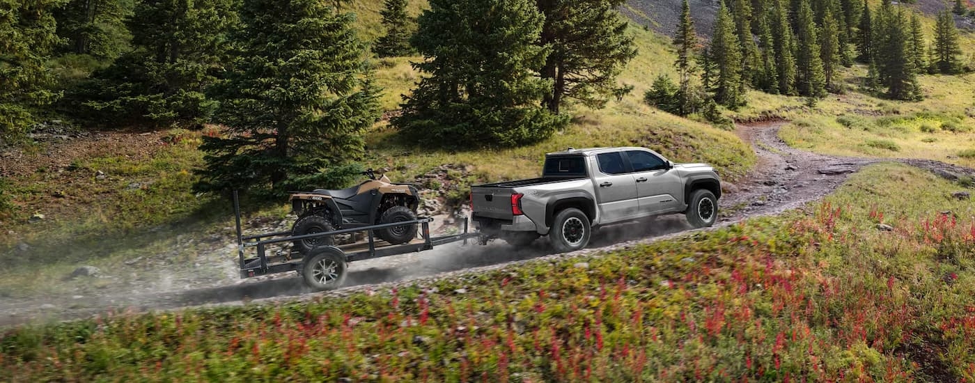 Grey 2025 Toyota Tacoma towing an ATV on a gravel trail