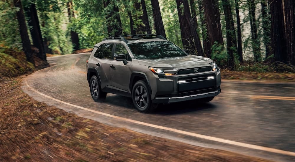 Grey 2026 Toyota RAV4 driving on a winding road through the woods