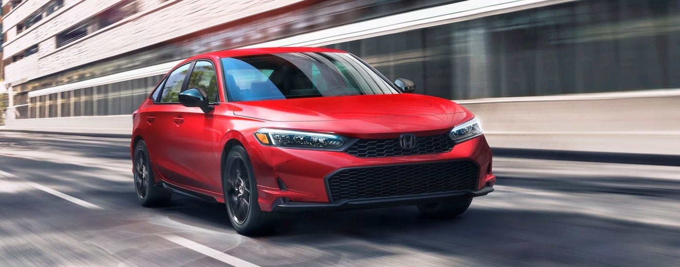 Red 2026 Honda Civic Sport for sale driving down an open road.