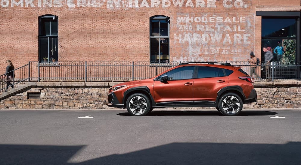 Side of an orange 2025 Subaru Crosstrek Limited parked near a brick wall.
