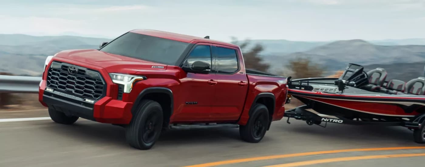 Red 2025 Toyota Tundra towing a boat down a road.