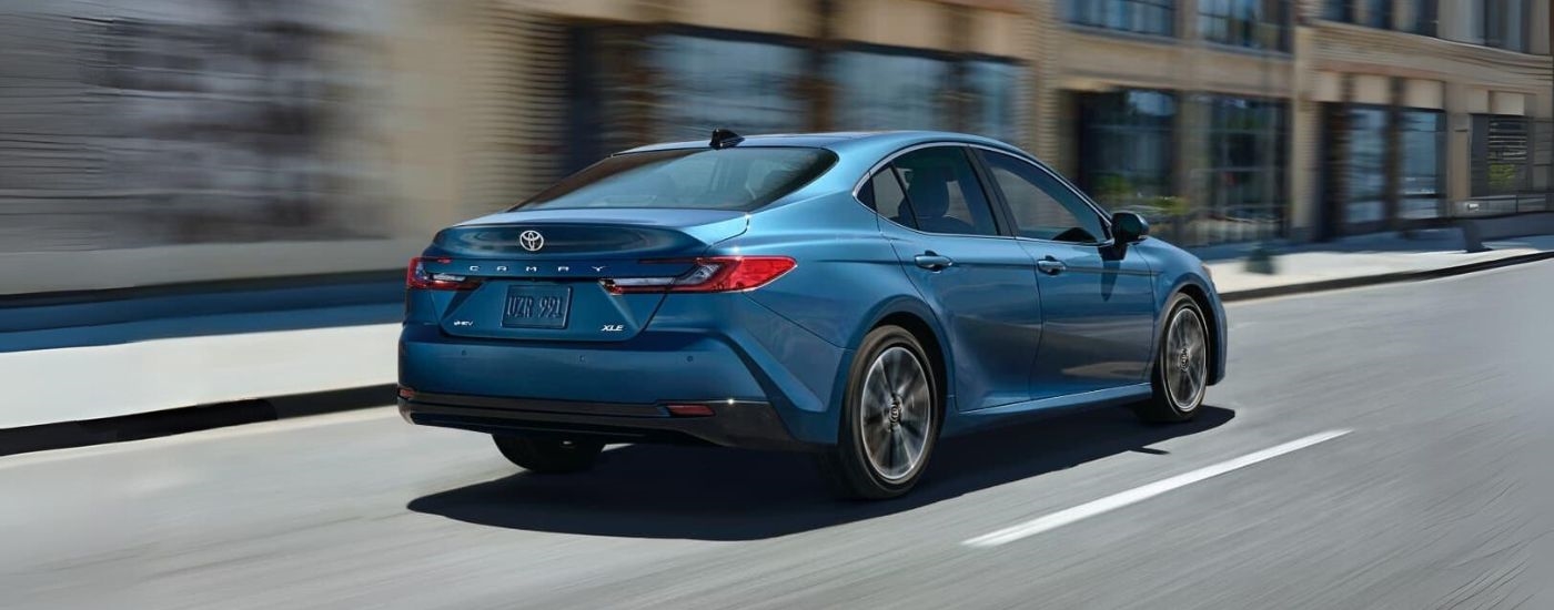 Rear of a blue 2025 Toyota Camry for sale near Mount Vernon driving down a road.