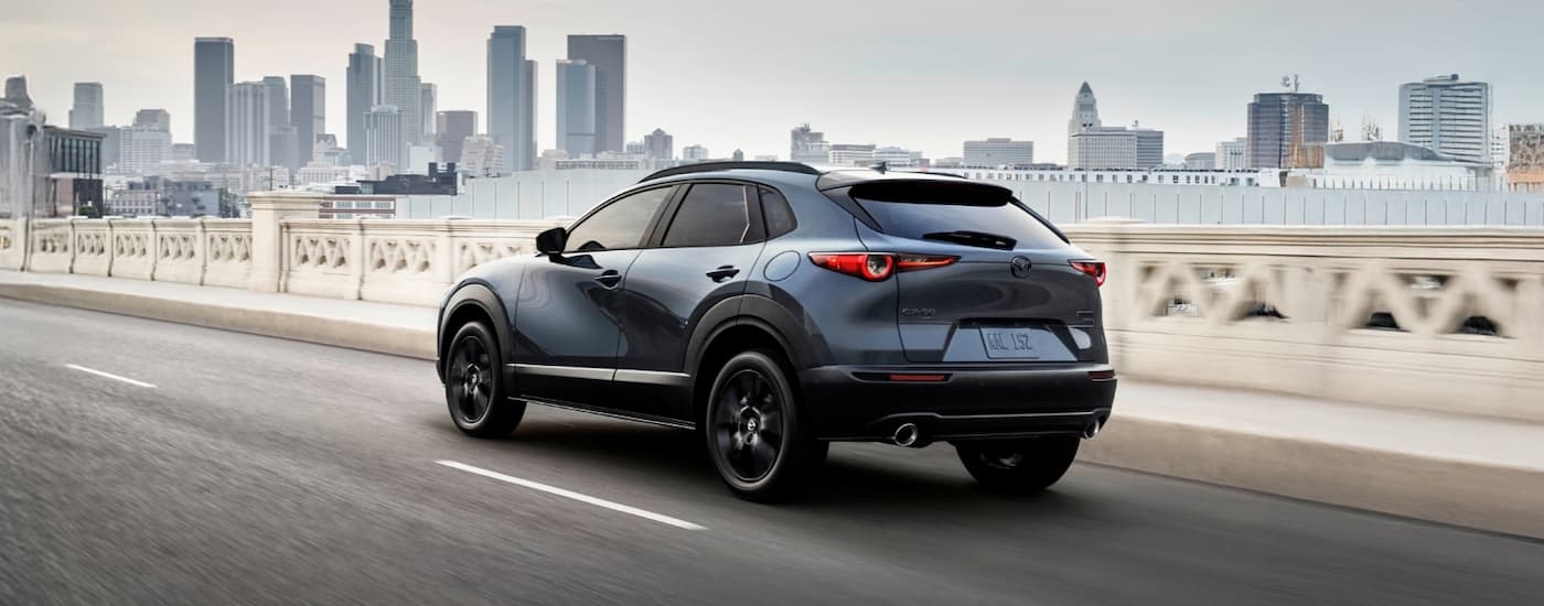 Rear of a dark blue 2026 Mazda CX-30 driving across a bridge.
