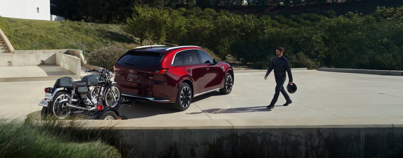 Person walking towards the rear of a red 2026 Mazda CX-90 Hybrid.