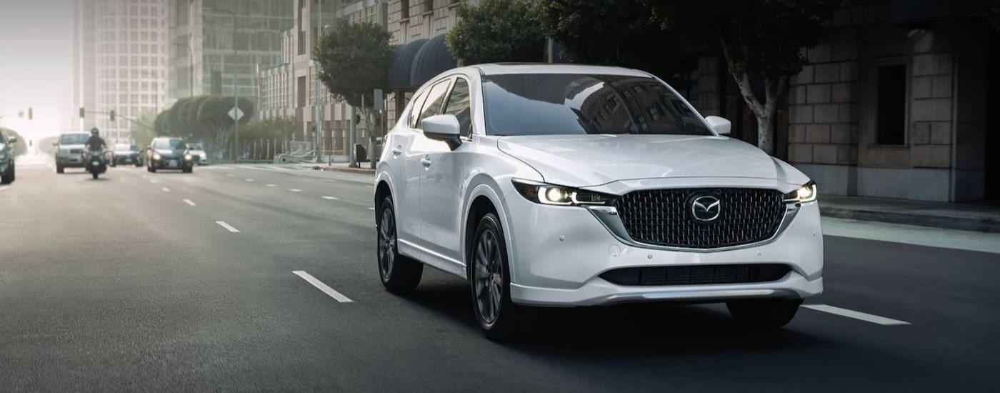 White 2025 Mazda CX-5 for sale near the Woodlands driving through a city.