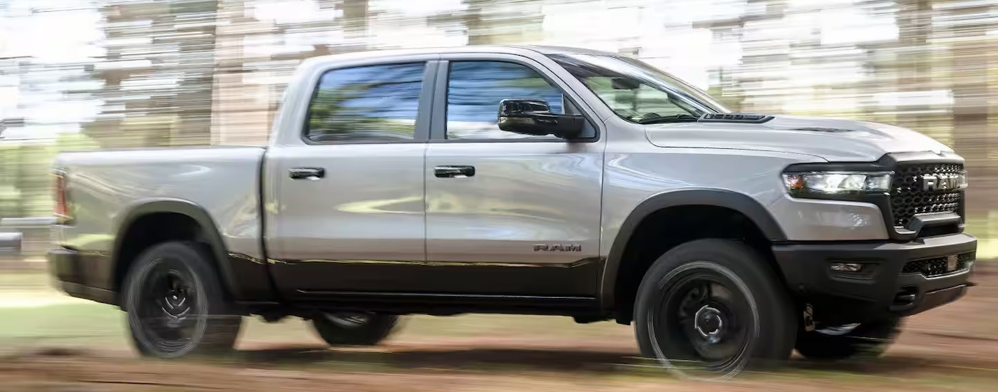 Side of a white 2025 Ram 1500 driving off-road through a forest.