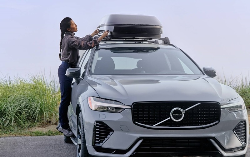 Volvo XC60 parked by the coast as a person attaches storage to the roof of car
