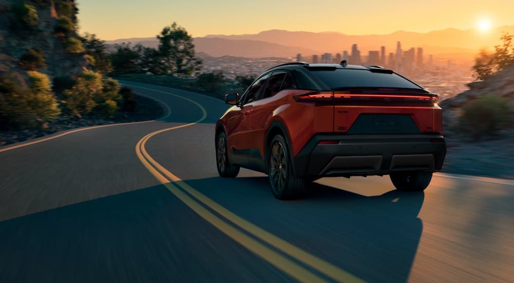 Rear of a red 2025 Toyota C-HR driving down a road.